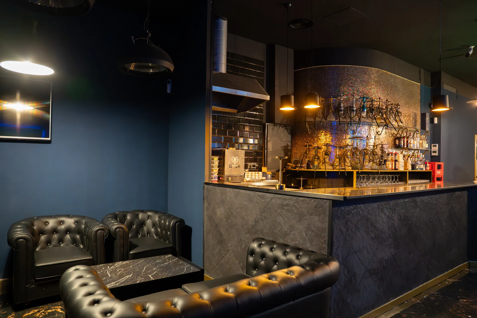 The Oceans bar, with bottles and shishas on its shelves, beside black chesterfield armchairs