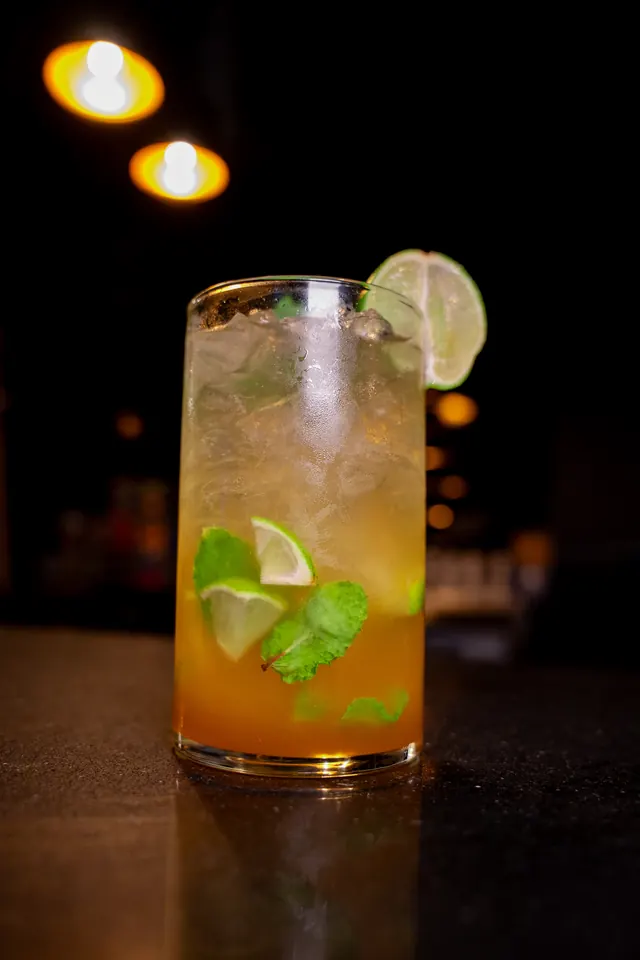 An amber cocktail with lime, mint and crushed ice in a tall glass