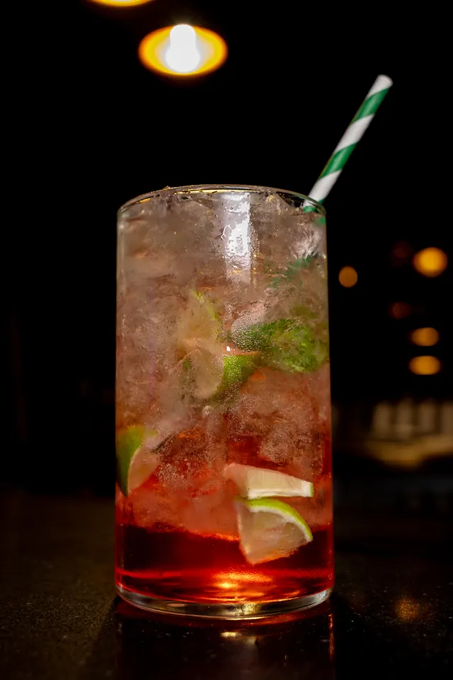 A red cocktail with lime, mint, crushed ice and a striped straw
