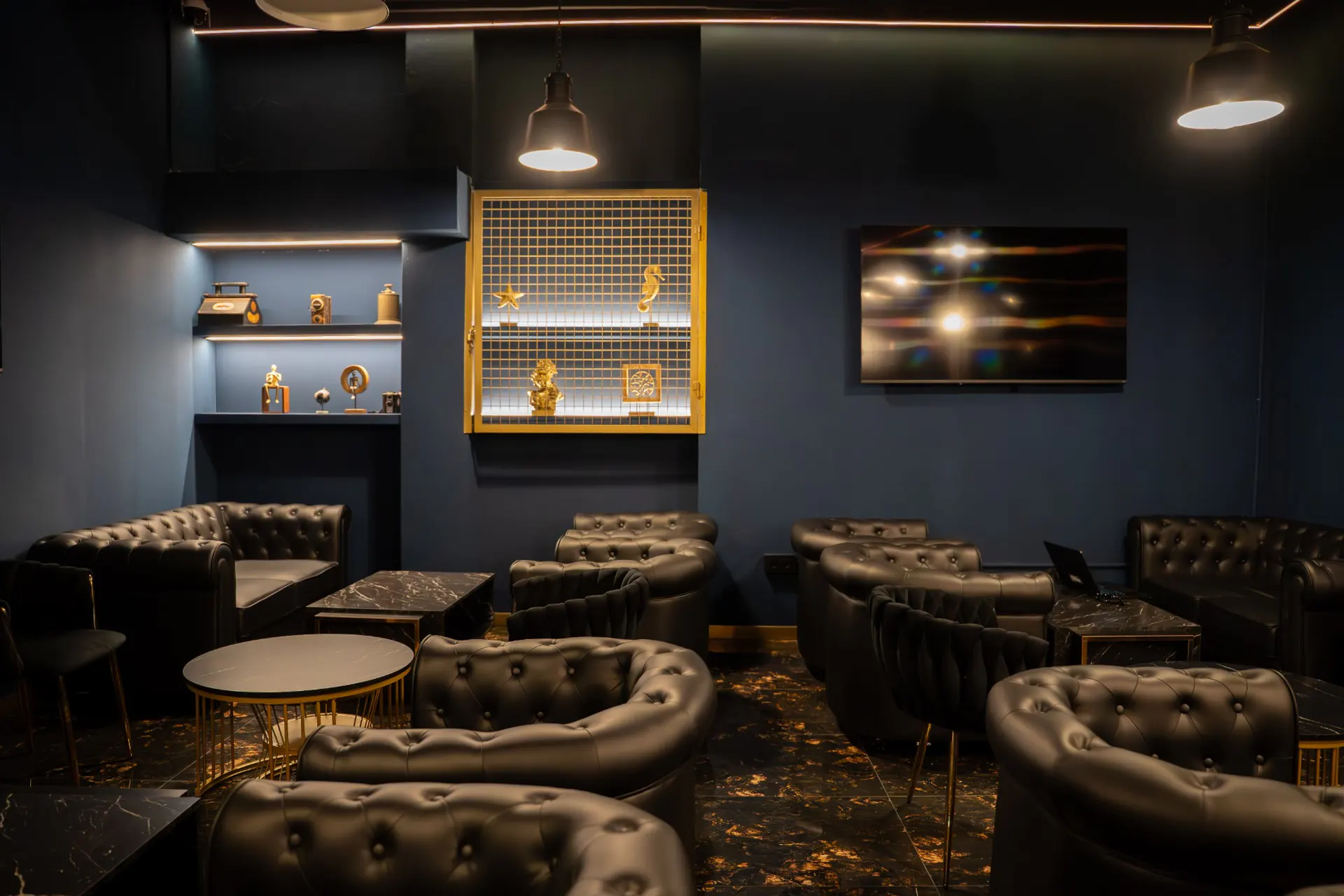 La sala de Oceans: sillones chester negros y mesas de mármol, estanterías iluminadas, una vitrina dorada y una pantalla en la pared azul marino